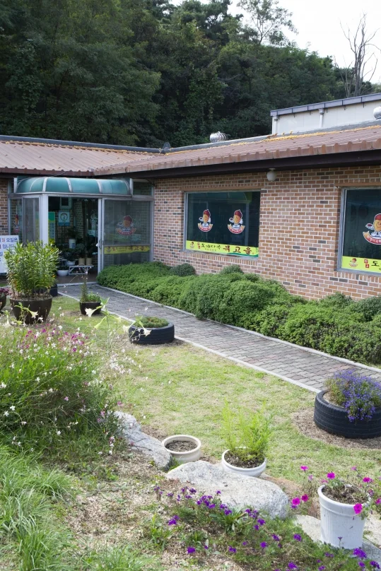 식당 앞 정원과 돌길, 화분과 꽃, 뒤로 식당 건물과 숲