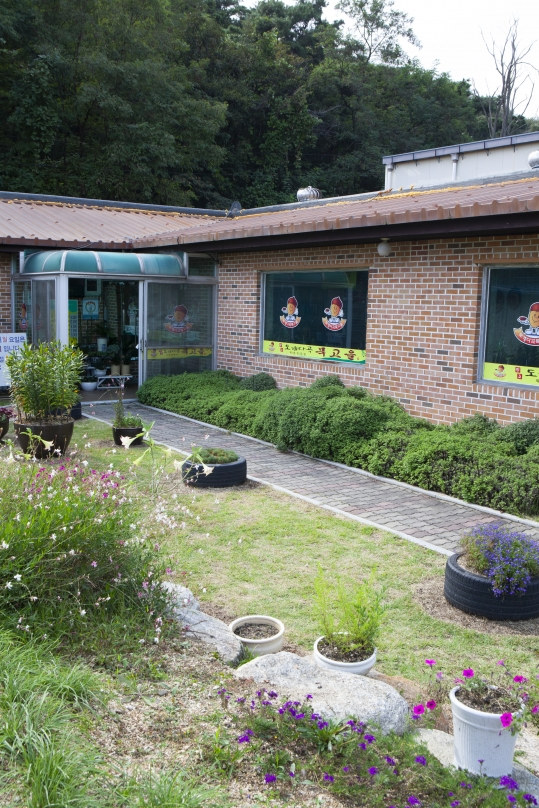 식당 앞 정원과 돌길, 화분과 꽃, 뒤로 식당 건물과 숲